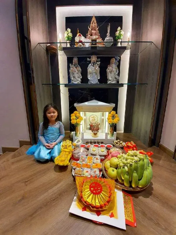 ลูกสาวกับ ตี่จู้เอี๊ยะ หินอ่อน 27 นิ้ว บ้านคุณสุขใจ พร้อมชุดเครื่องไหว้ ผลไม้ กระดาษทองจีน ด้านหลังมีพระพุทธรูป และ รูปปั้นเทพจีน